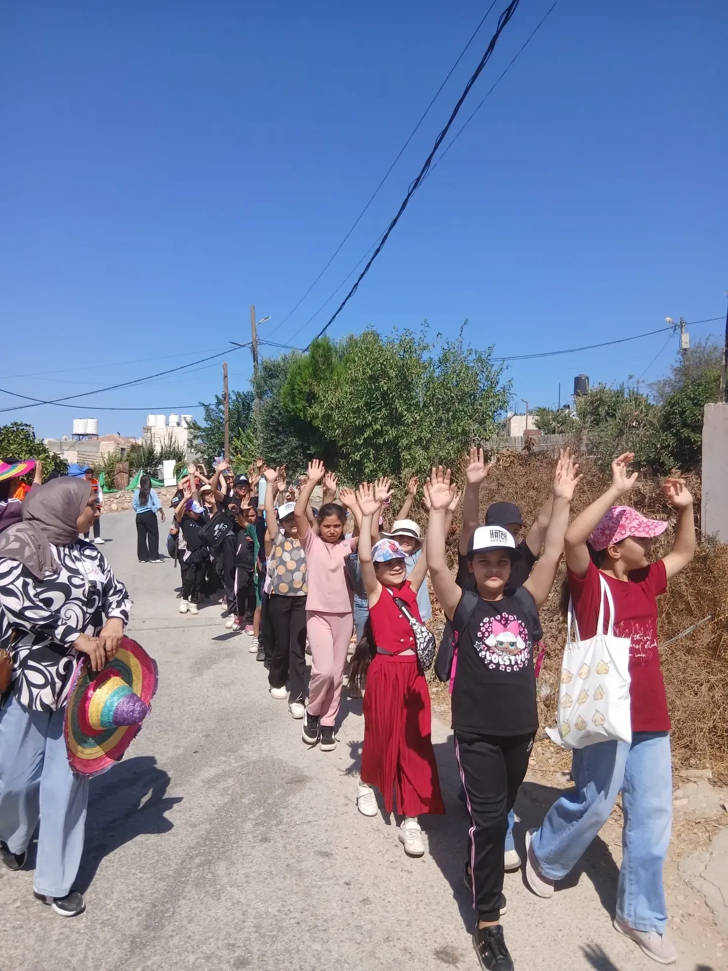 Children walking in a line with their hands raised during the Vita Creative camp in Beit Ummar