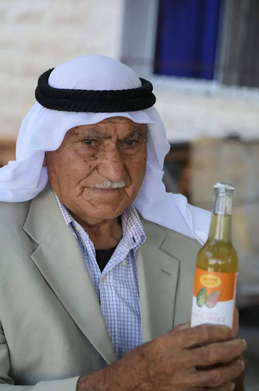 رجل مسنّ يرتدي الكوفية والعقال ويحمل زجاجة من عصير صبر